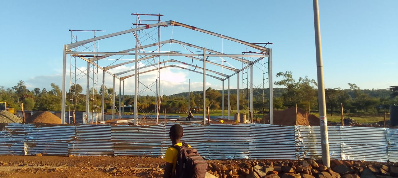 Steel portal frame structure under construction, viewed from the site access road